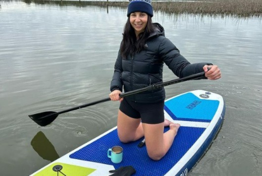 Kristin wearing her macpac jacket while stand up paddle boarding and having a morning brew